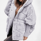 A woman wearing a light gray puffer jacket with plush faux-fur trim and ribbed knit sleeves, shown against a plain white studio background.