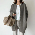 Person wearing a gray cardigan holding a beige handbag on a plain background