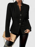 Person wearing a black blazer holding a beige clutch against a neutral background