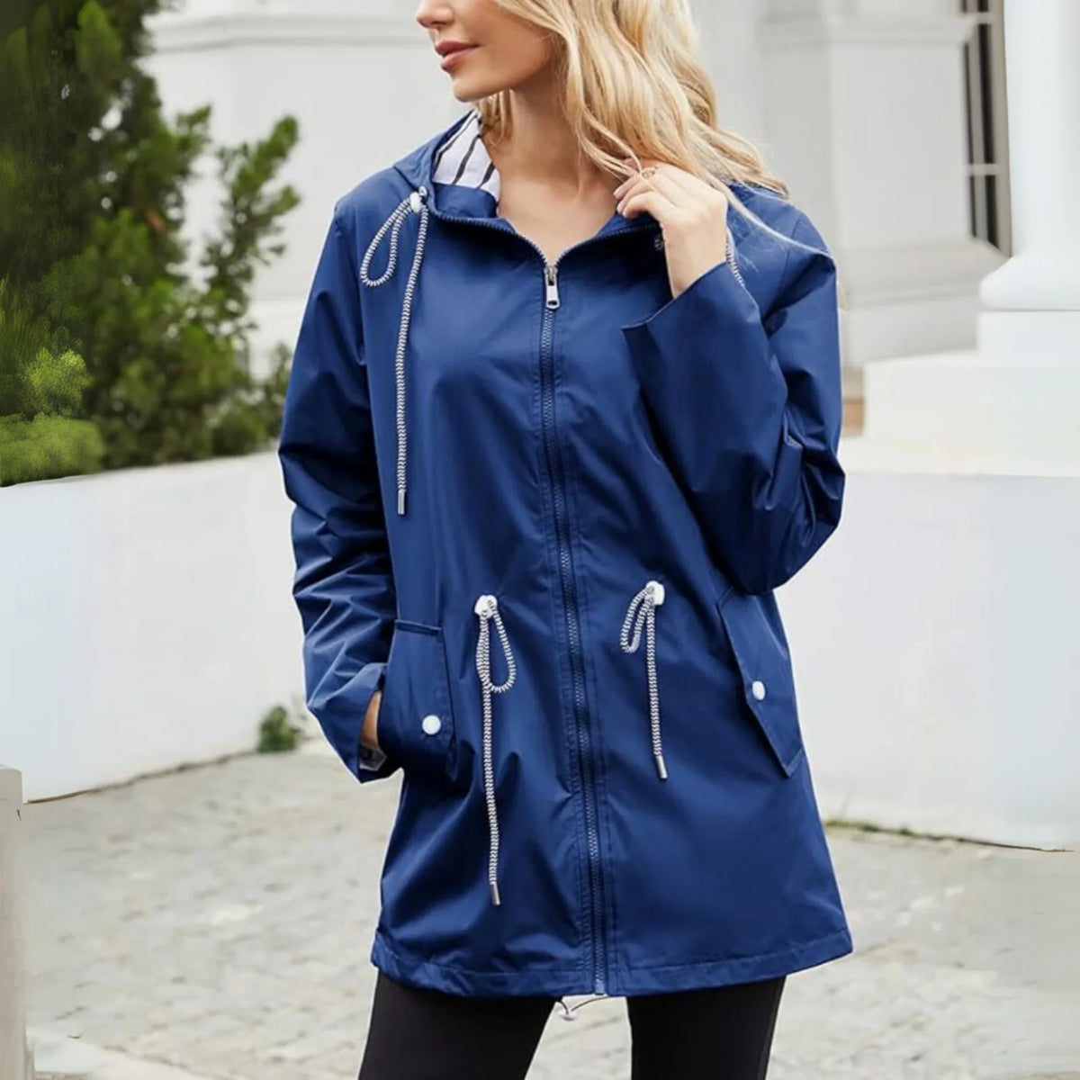 Woman wearing a blue raincoat with white drawstrings in an outdoor setting.
