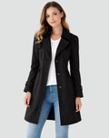 Woman wearing a black coat over a white shirt and blue jeans on a light gray background