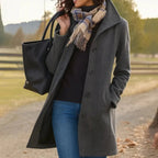 Woman wearing a gray coat with a black bag and plaid scarf outdoors.