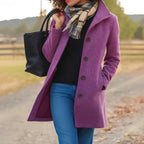 Person wearing a purple coat with a black handbag and plaid scarf outdoors.