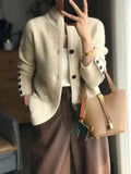 Person wearing a beige textured jacket with black buttons, holding a brown handbag.