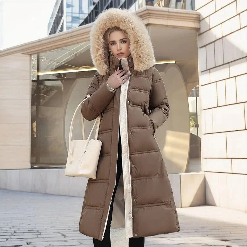 Woman wearing a long brown puffer coat with a fur-lined hood in an urban setting.