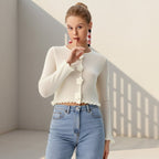 Woman wearing a white cardigan with floral details and blue jeans in a minimalistic setting
