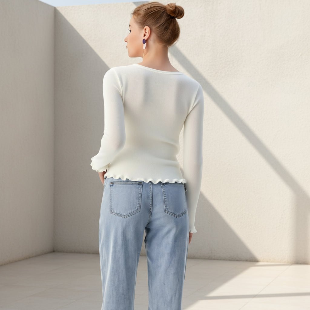 Woman wearing a white sweater and light blue jeans on a plain background