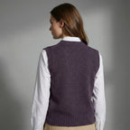 Woman wearing a purple knitted vest over a white shirt on a gray background