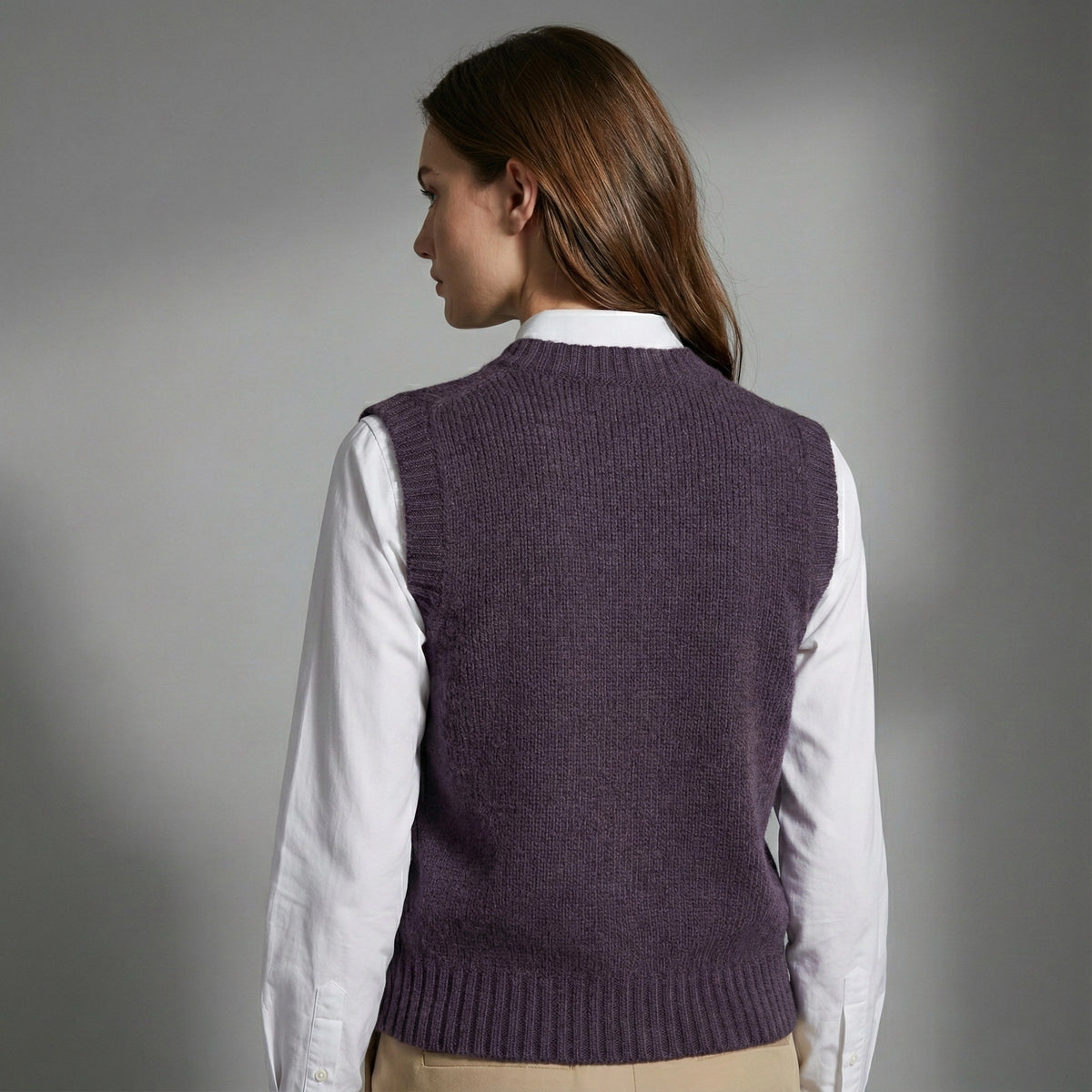 Woman wearing a purple knitted vest over a white shirt on a gray background