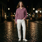 Woman wearing a striped shirt and white pants standing on a cobblestone street at night.