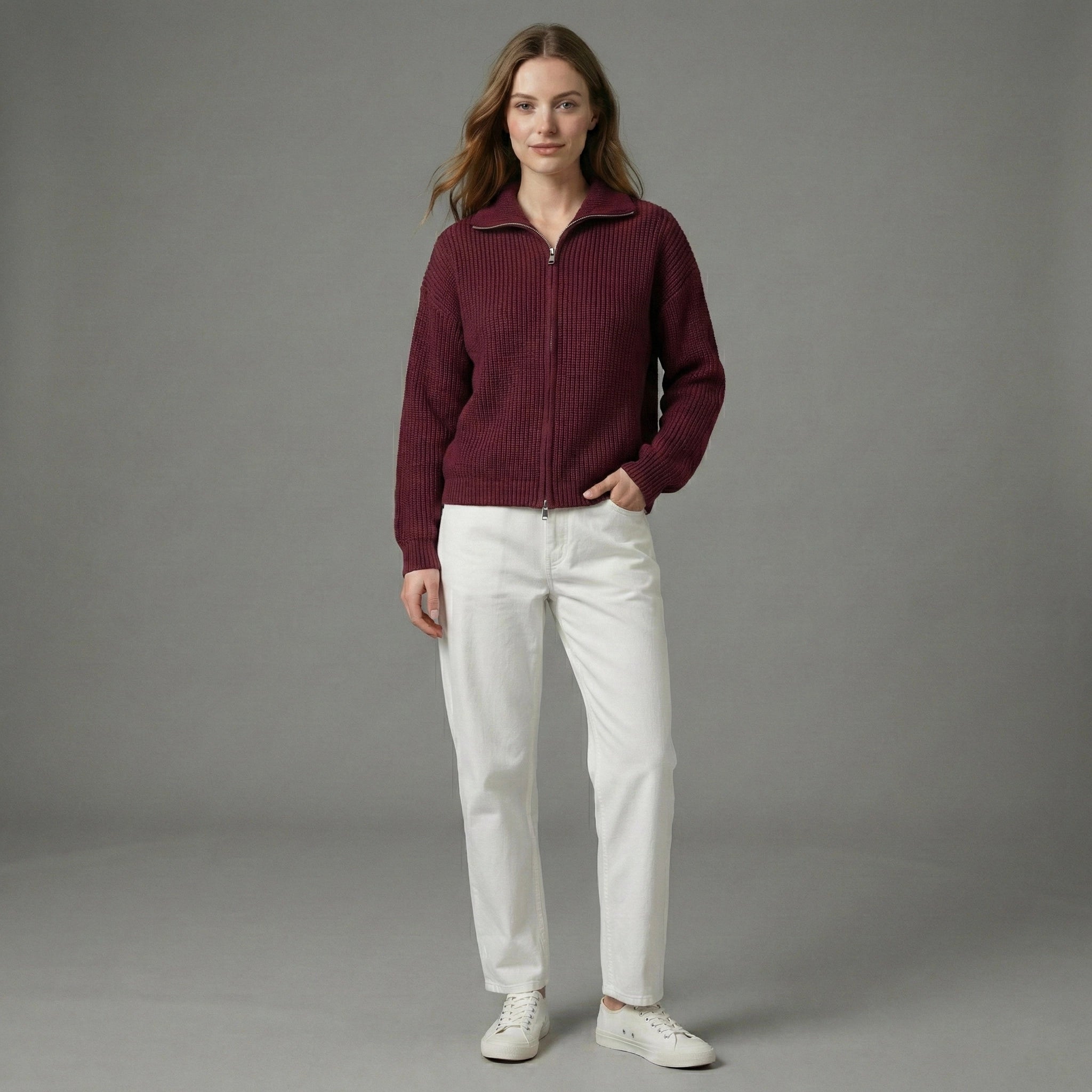 Woman wearing a burgundy jacket and white pants against a gray background